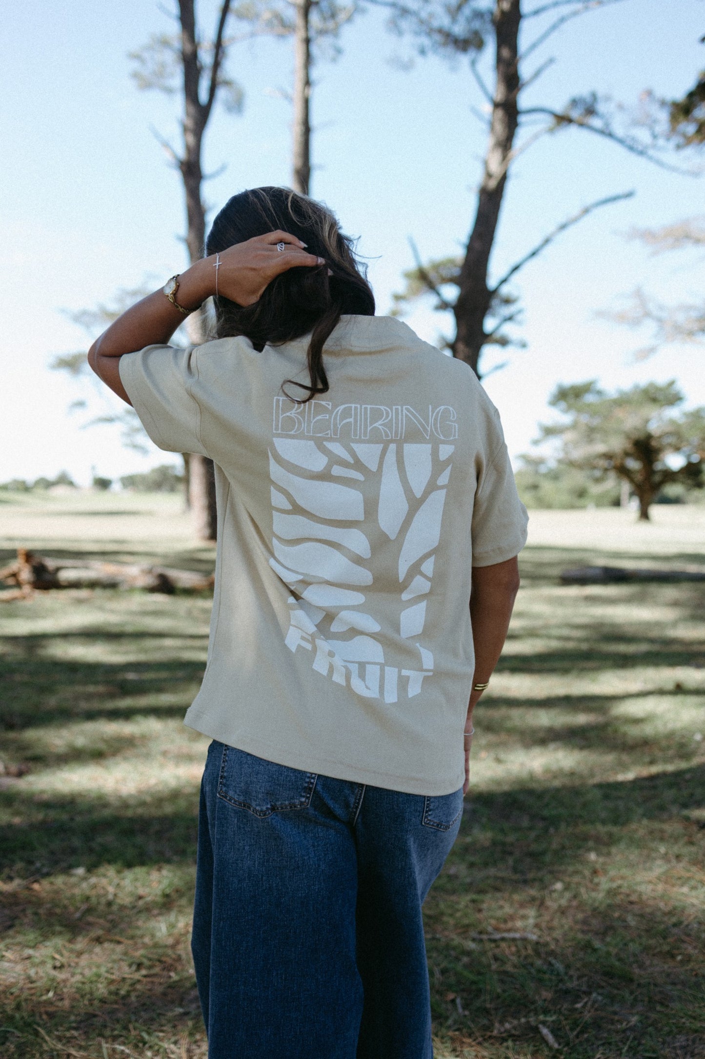 Person wearing a beige Bearing Fruit t-shirt with a graphic design outdoors