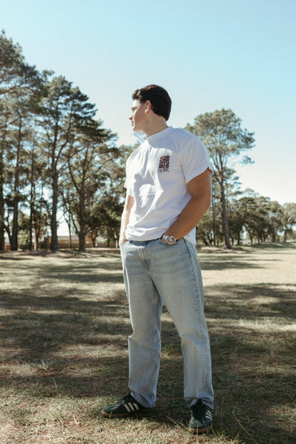 Person wearing a white Born again oversized T-shirt with a logo and light blue jeans standing in a grassy area with trees.