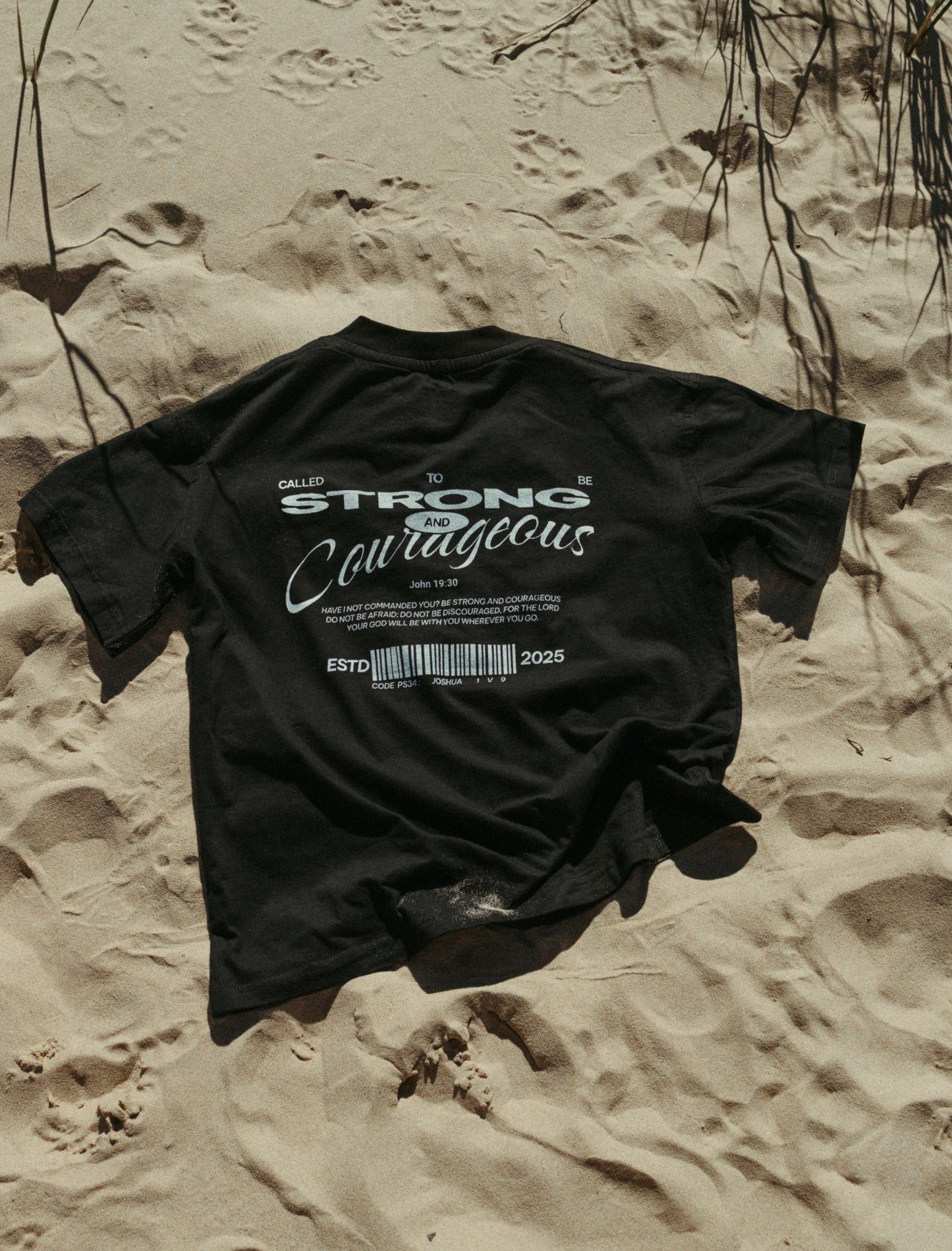 Black oversized Christian t-shirt with text on sand in Port Elizabeth, Eastern Cape, South Africa